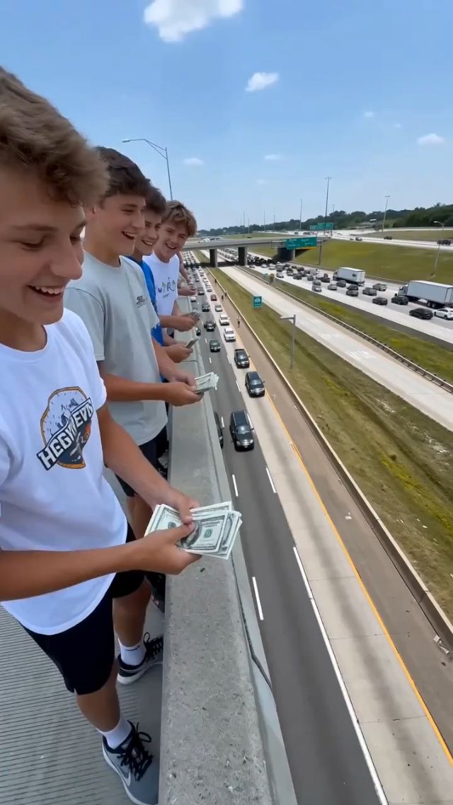 young men throw cash from the bridge down to the highway, causing cars to stop and hit each other. Static shot, 50mm lens, with a slight ...